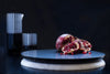 A marble serving board black marble face up with an open pomegranate  placed on it, photographed on a black background, with styled glassware out of focus in the background