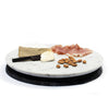 A marble serving board with a piece of cheese, prosciutto, and nuts placed on it, photographed on a white background.