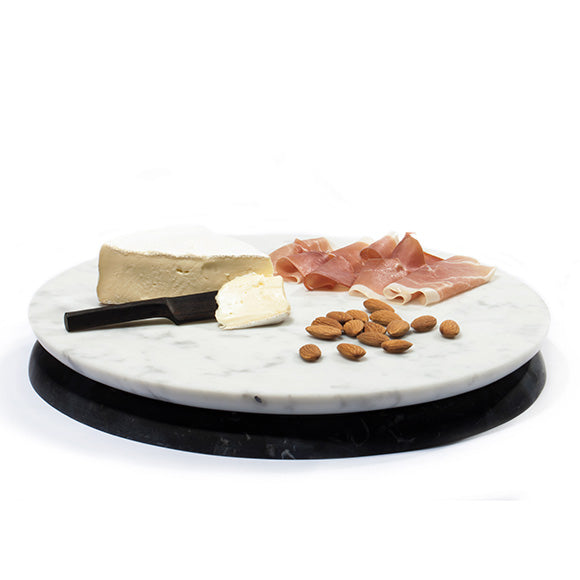 A marble serving board with a piece of cheese, prosciutto, and nuts placed on it, photographed on a white background.